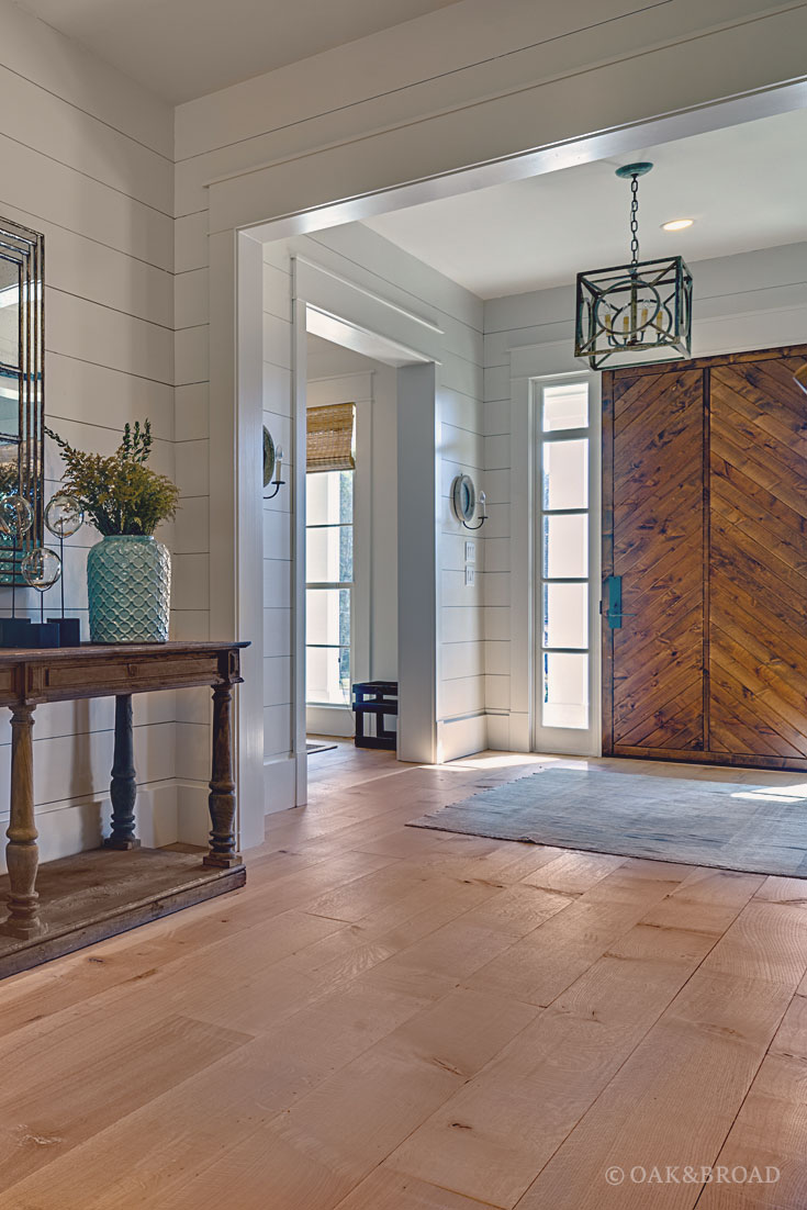 Wide Plank White Oak Hardwood Floor by Oak and Broad with Custom Stain | Rustic modern entryway showing teal flower pot, iron-style chandelier, rug, and natural light